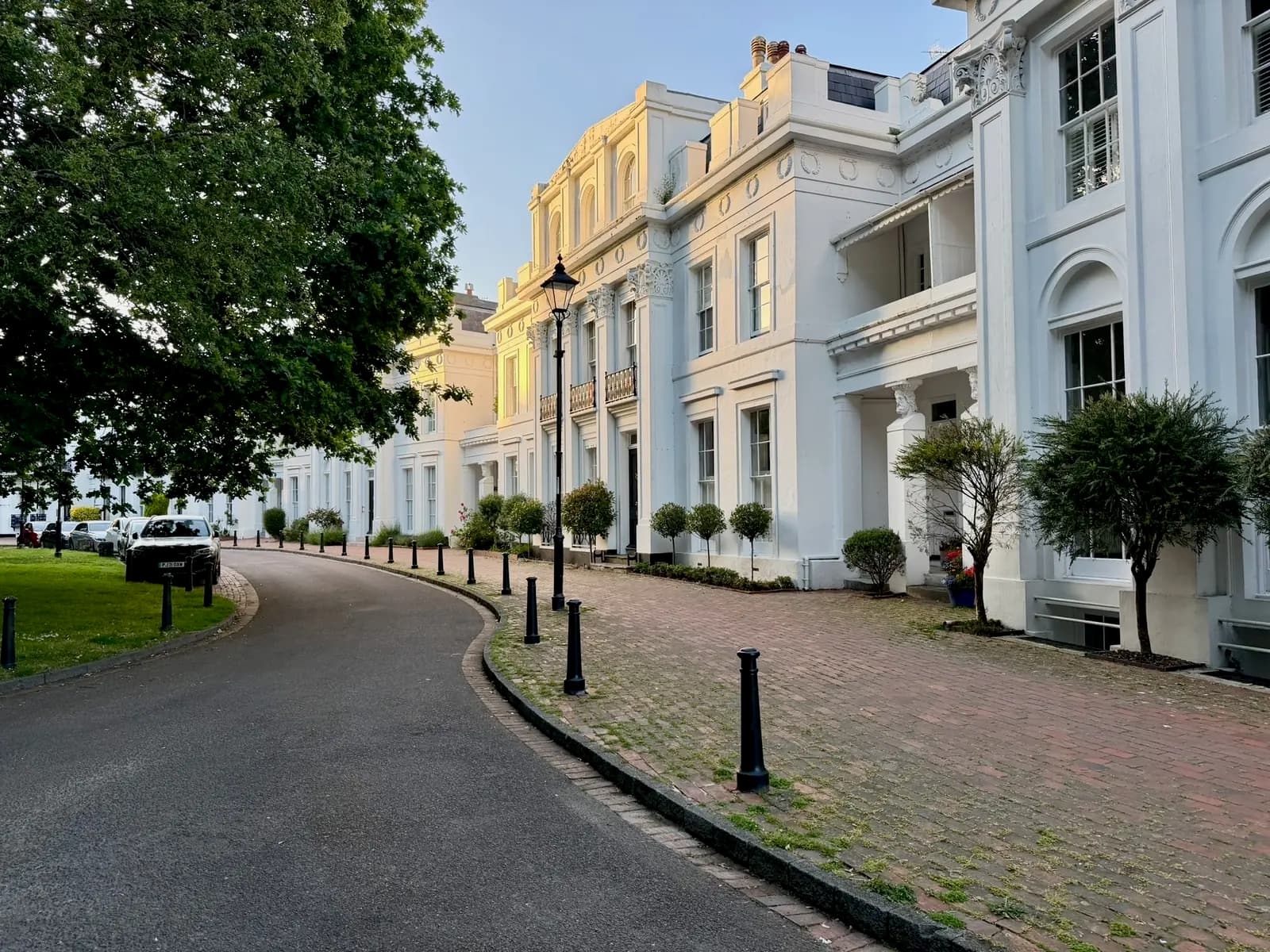 A row of grand cream-stuccoed terraces lining a curved tree-shaded driveway in Heene