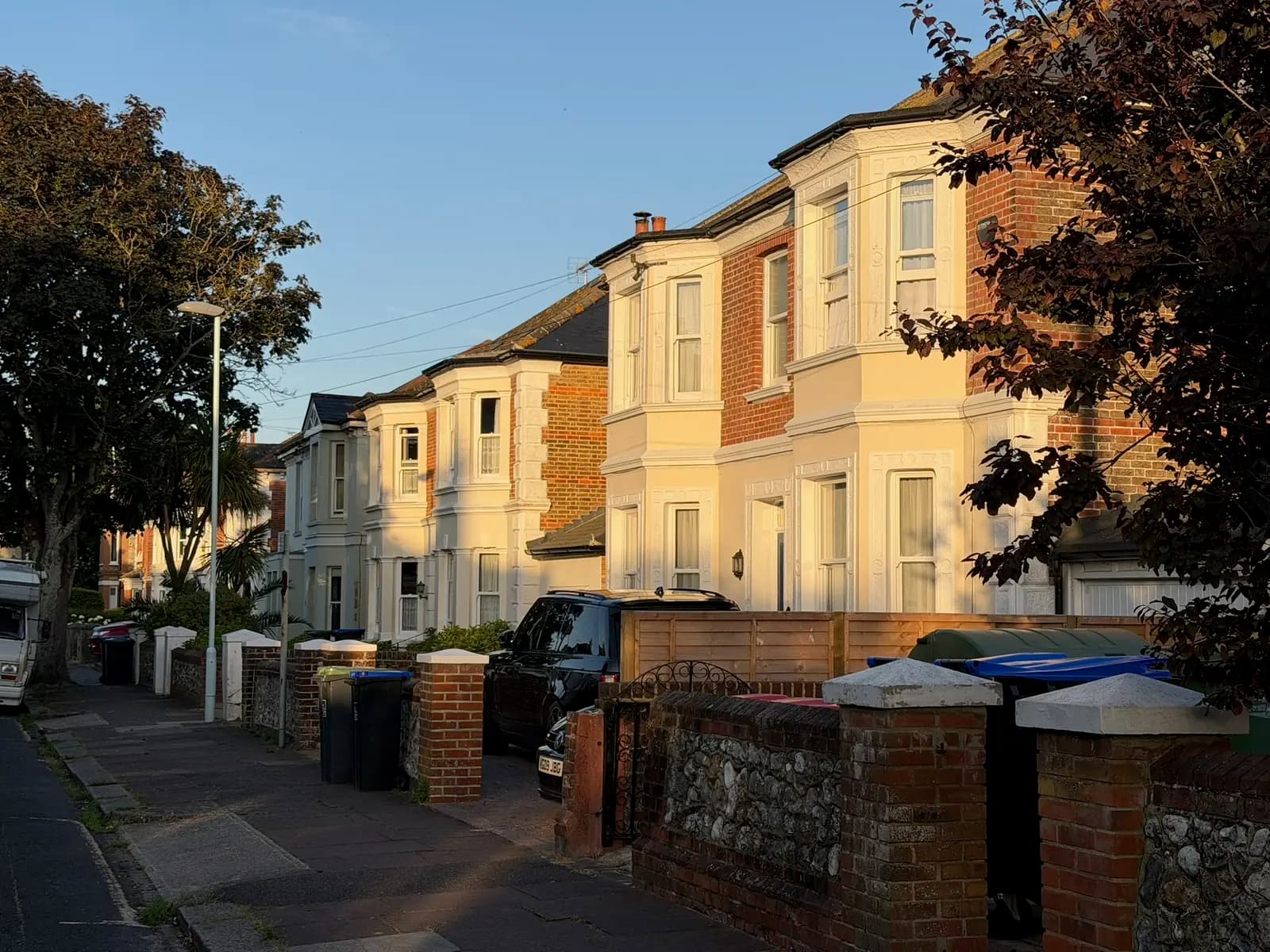 A row of cream-painted Victorian semi-detached villas with bay windows in golden-hour sunlight