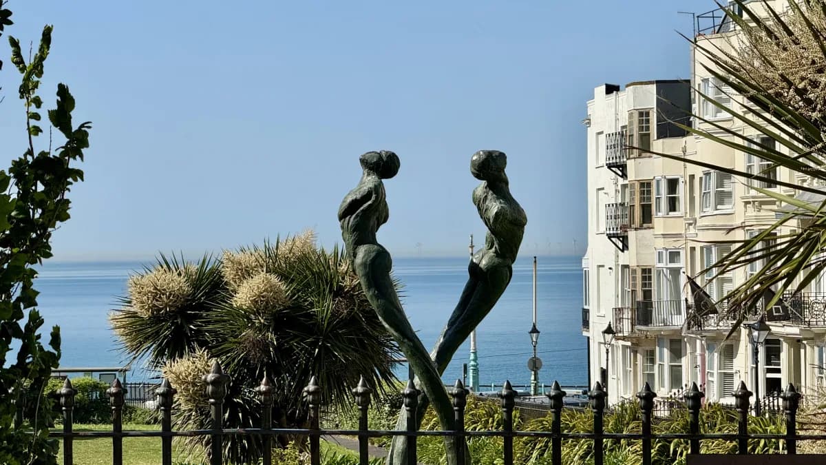 A bronze sculpture of two figures in seafront gardens, with a Regency apartment block behind