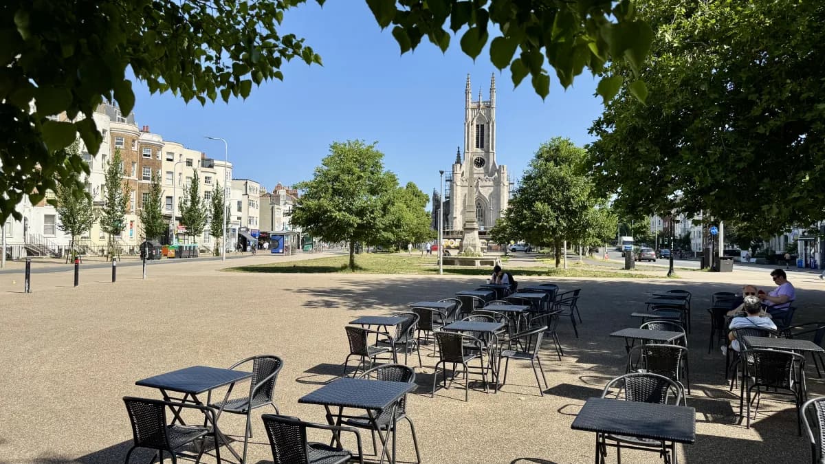 Cafe tables on the Old Steine with St Peter's Church spire rising behind the trees