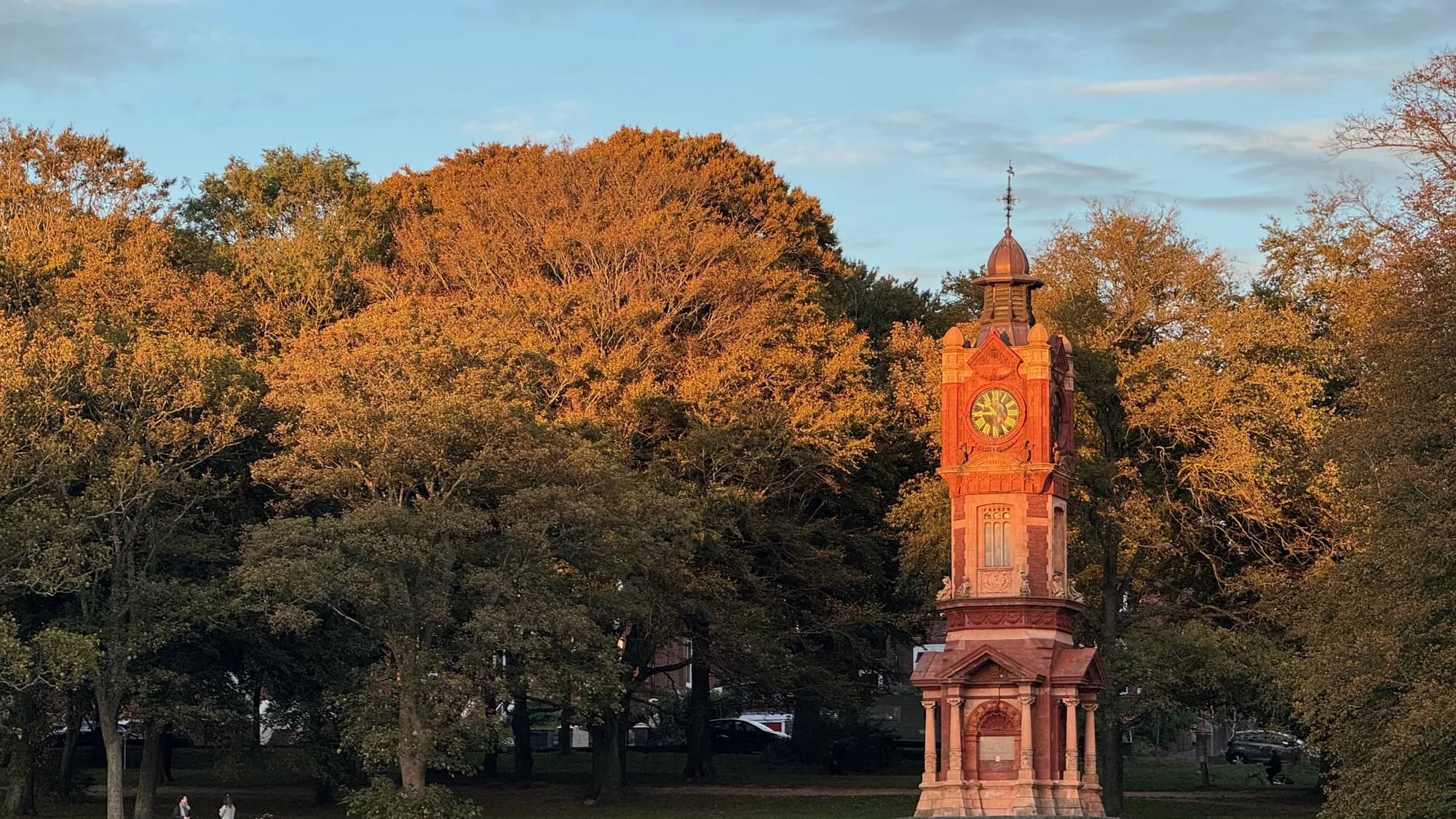 The Preston Park clock tower lit by low autumn sun against autumn-coloured trees