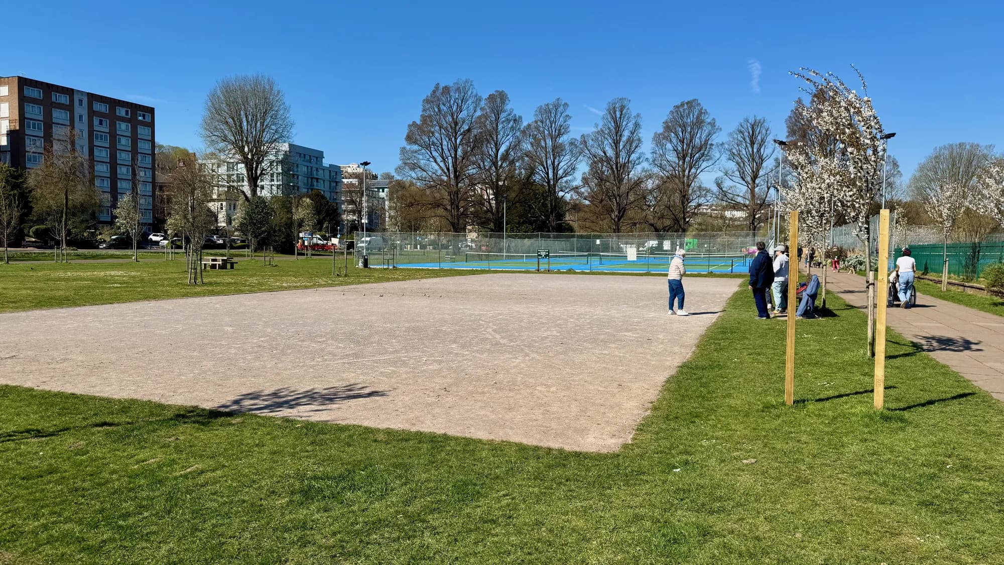People playing petanque on the boules pitch in Preston Park, with the Brighton skyline behind