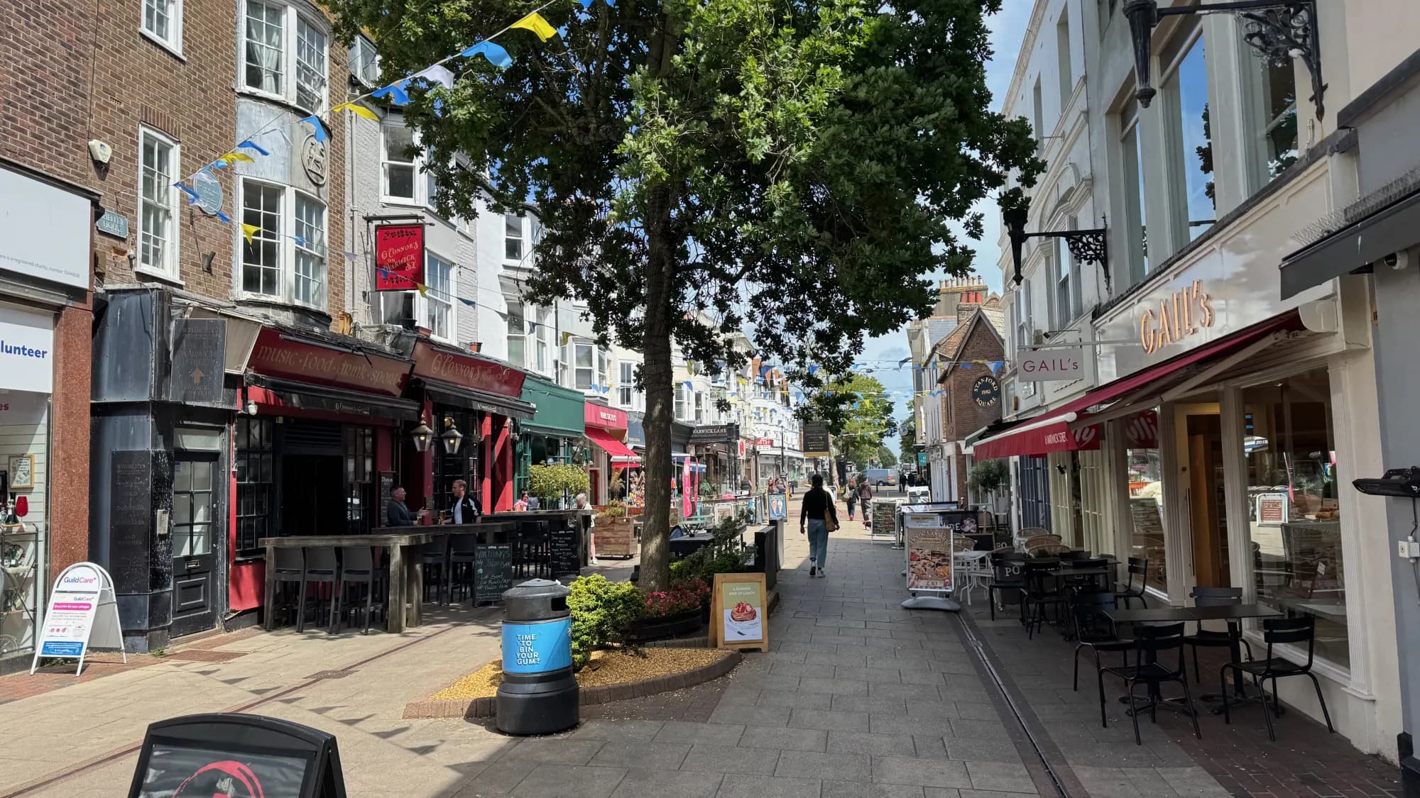 Independent cafés and restaurants spilling onto a pedestrianised town-centre street under summer bunting